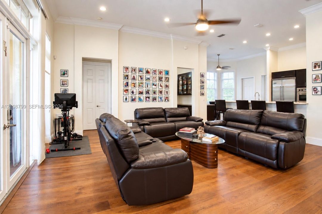 Open-concept interior featuring wood-finish flooring, recessed lighting, crown molding, double glass doors, and a breakfast bar