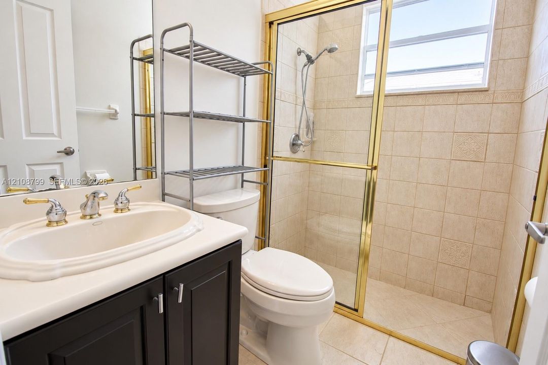 Bathroom featuring a dark wood-finish vanity, integrated oval sink, brass-tone hardware, shower enclosure with glass sliding doors, and tiled wall finishes