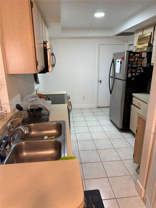Kitchen featuring neutral cabinetry, stainless steel appliances, double-basin stainless steel sink with high-arc faucet, and light-toned tile flooring