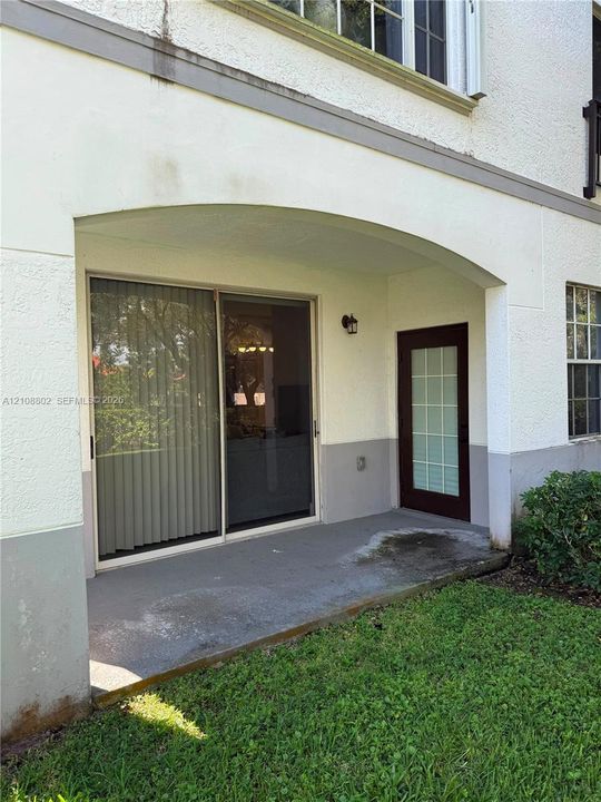 Covered concrete patio featuring a sliding glass door, a separate exterior door with glass panes, and an attached wall-mounted light fixture