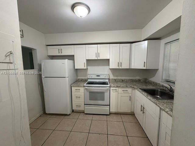 Kitchen featuring white shaker-style cabinetry, speckled stone-finish countertops, stainless steel sink with a metallic faucet, ceramic tile flooring, and integrated white appliances