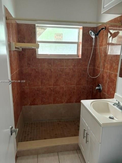 Shower enclosure featuring earth-tone tiled walls, a small-format tiled floor, an adjustable handheld shower fixture, and a built-in white vanity with an integrated sink