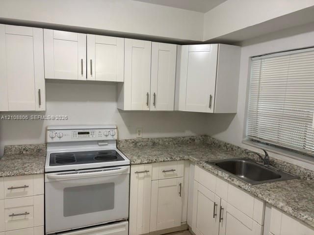 Kitchen featuring white shaker-style cabinetry, speckled stone-finish countertops, stainless steel sink with metal faucet, and a white freestanding electric range