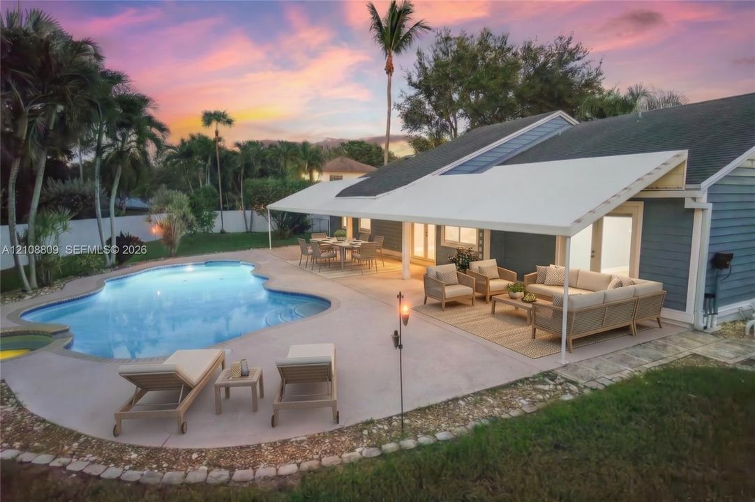 Custom-shaped inground swimming pool with a sprawling concrete patio, expansive covered lanai, and solid-color siding exterior