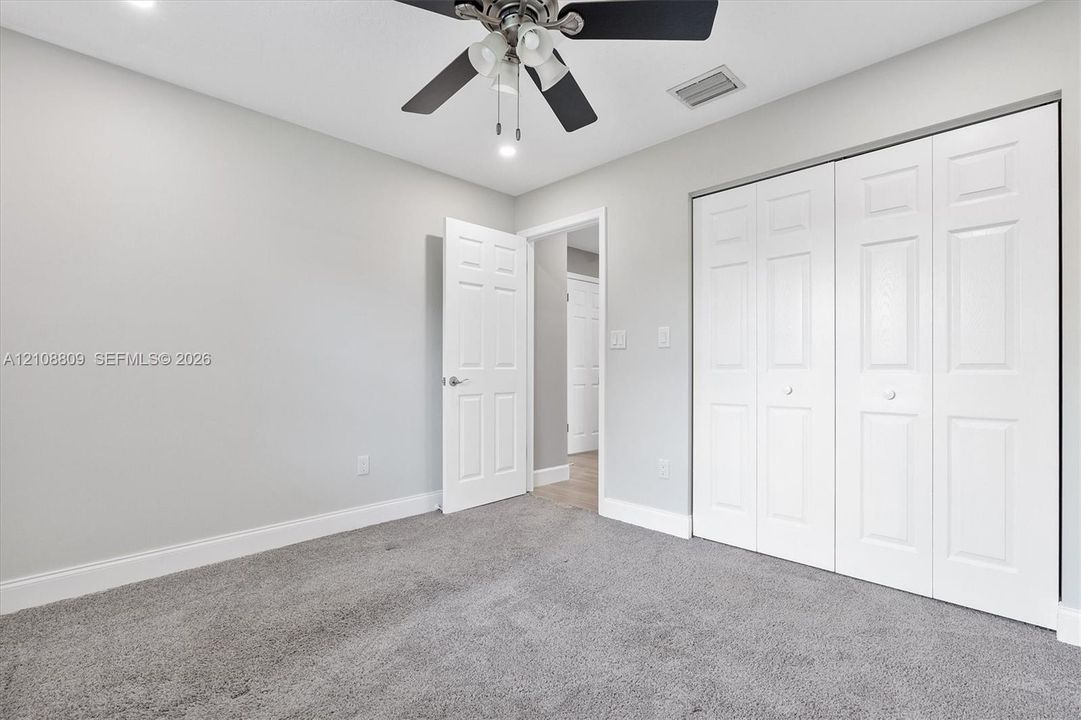 Interior room featuring neutral-tone carpeting, a multi-panel door, a multi-panel closet door, and a ceiling fan with integrated lighting
