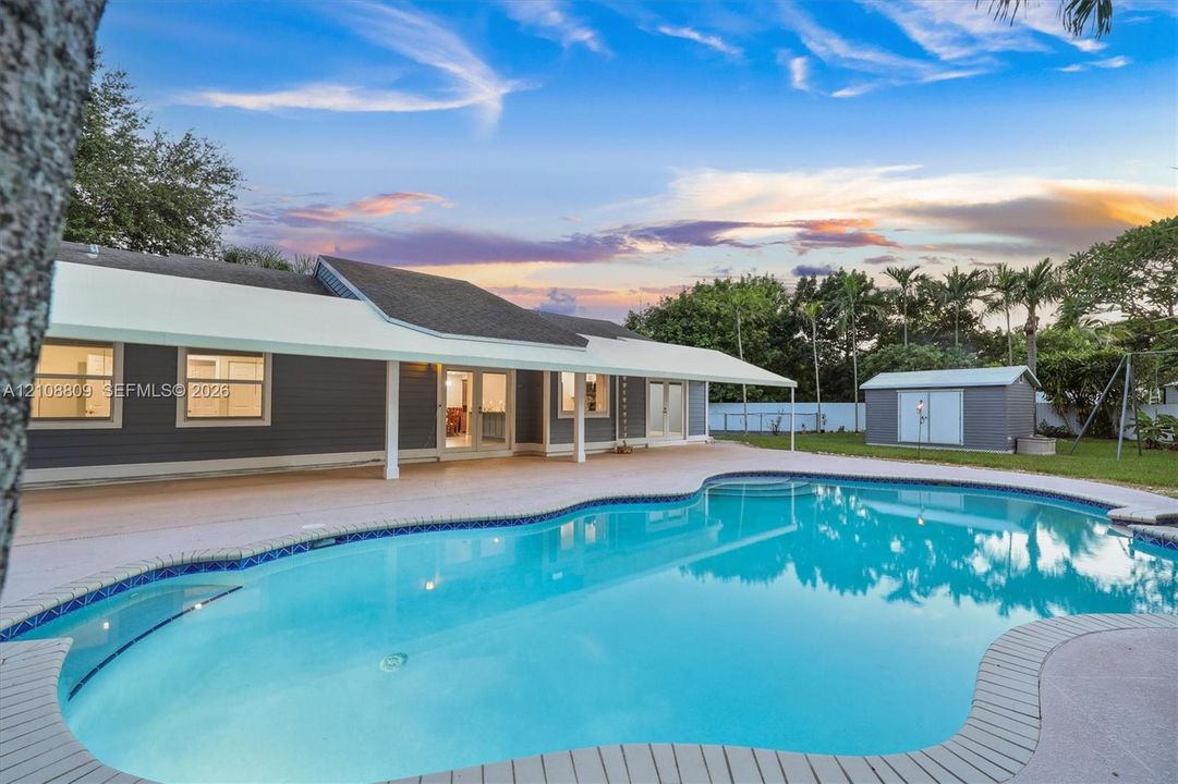 Rear exterior featuring a freeform swimming pool, extensive concrete patio, covered lanai, lap siding, and multi-pane glass doors