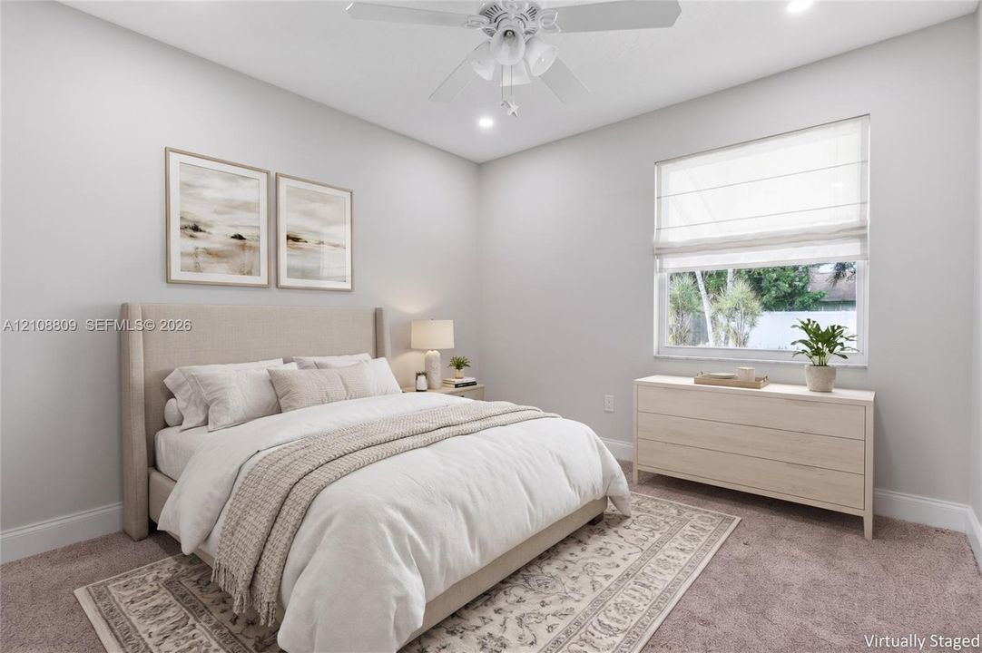 Neutral-toned interior space featuring carpeting, a white ceiling fan with integrated lighting, and a single-pane window with a Roman shade