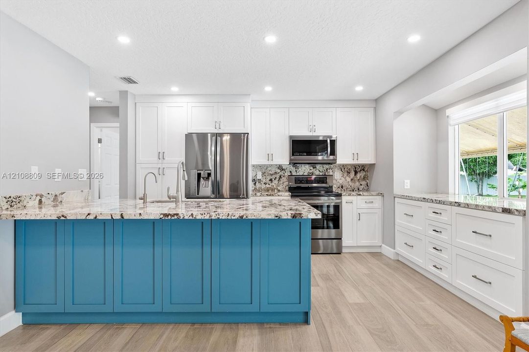 Kitchen featuring a blue-accented center island, white cabinetry, stone-finish countertops, stainless steel appliances, and wood-finish flooring