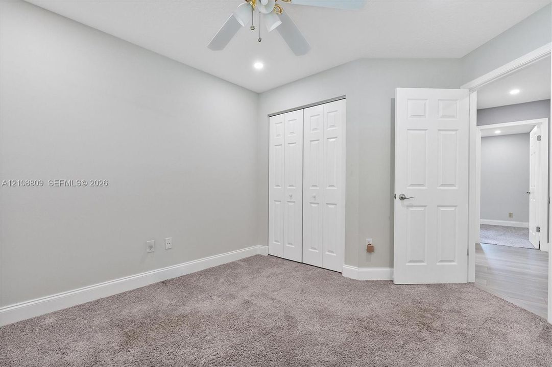 Neutral wall tones, carpeted flooring, bi-fold closet doors, six-panel interior door, and a ceiling-mounted light fixture with a fan