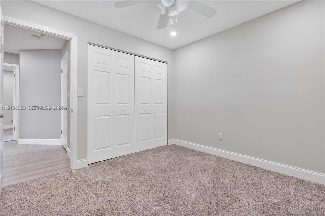 Neutral-toned wall paint, plush carpeting, ceiling fan with integrated lighting, and double-panel closet doors