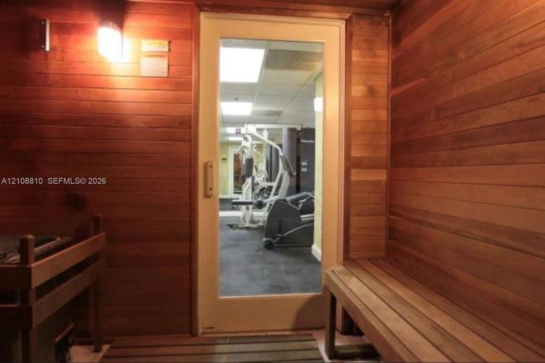 Sauna featuring wood paneling, built-in tiered bench seating, a slatted wood floor, and an integrated glass-panel door