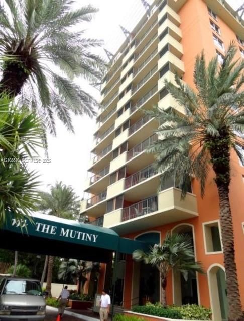 High-rise multi-story building featuring stacked exterior balconies with metal railings, a covered entrance awning, and structural arched entryways