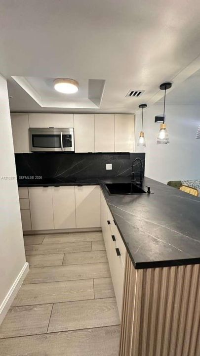 Kitchen featuring flat-panel cabinetry, dark stone-style countertops, integrated undermount sink, pendant lighting, and wood-finish flooring