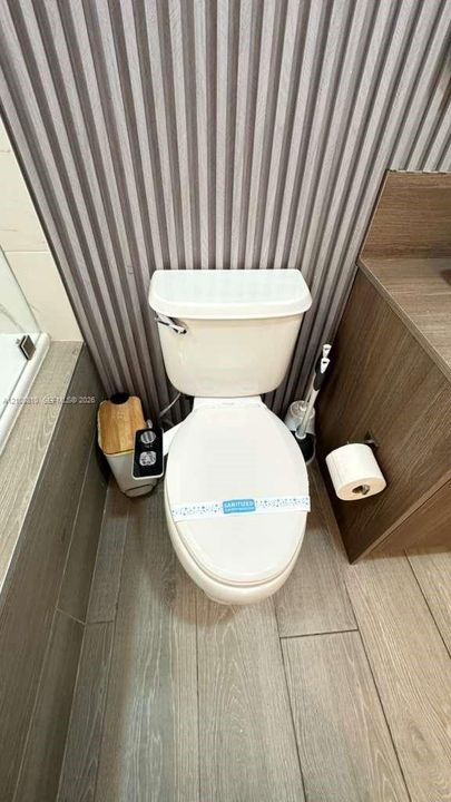 Bathroom featuring vertical wall paneling, wood-finish tile flooring, and a wall-mounted toilet paper holder