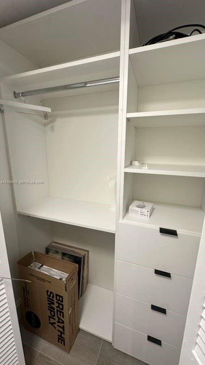 Built-in closet organizer featuring white shelving, a metal hanging rod, and four soft-close drawers with matte black hardware