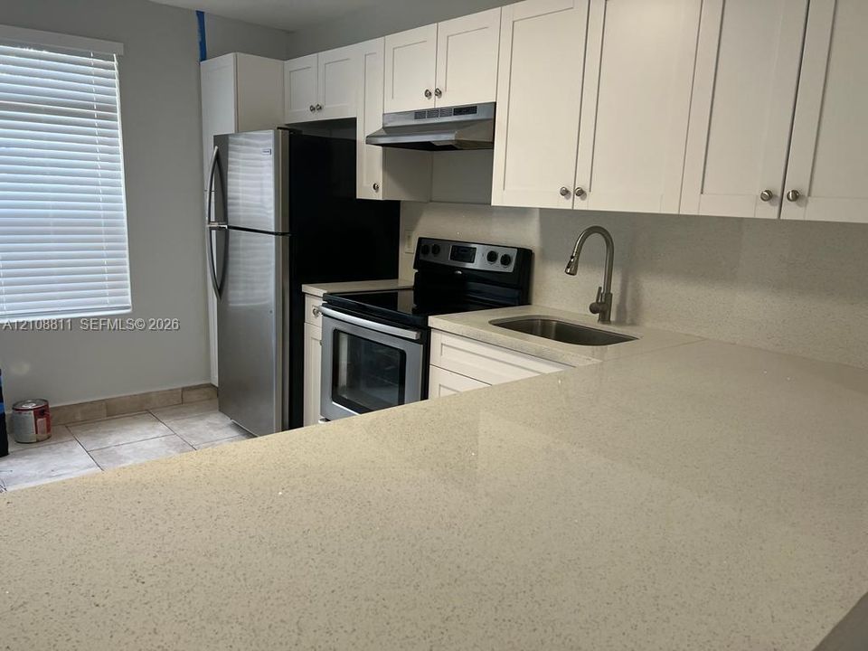 Kitchen featuring white shaker-style cabinetry, solid-surface countertops, a stainless steel undermount sink with a gooseneck faucet, and stainless steel appliances