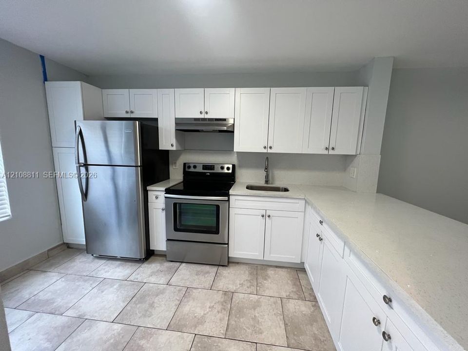 Kitchen featuring white cabinetry, solid surface countertops, stainless steel appliances, a stainless steel range hood, and tile flooring