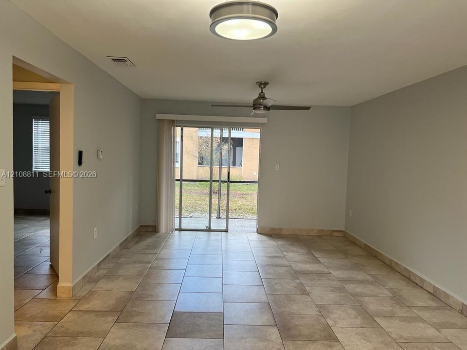 Large-format tile flooring, ceiling fan, flush-mount lighting, and glass sliding door access to exterior space