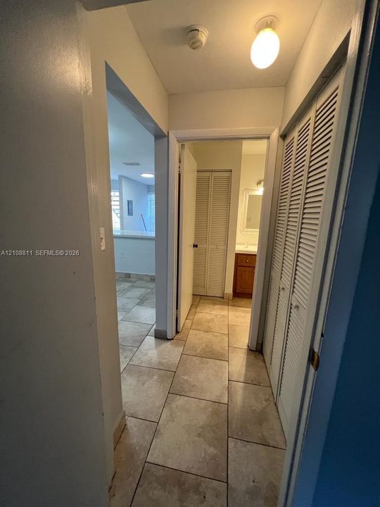 Interior corridor featuring large-format ceramic tile flooring, floor-to-ceiling bi-fold closet doors, and a flush-mount overhead light fixture
