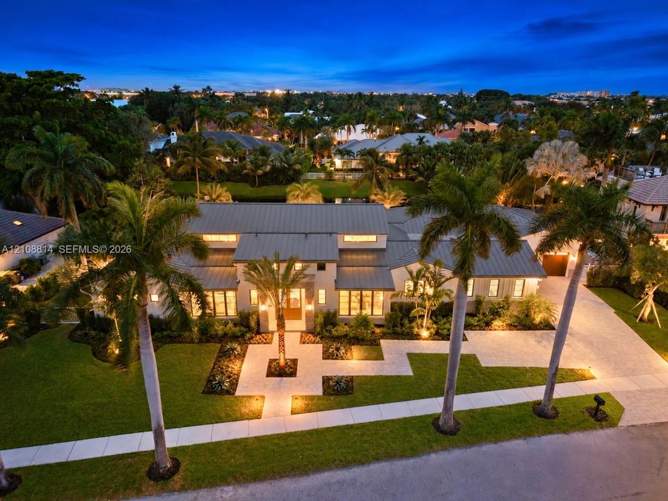 Modern residence featuring a standing-seam metal roof, paver driveway, manicured lawn, stone-surface entryway, and mature palm landscaping