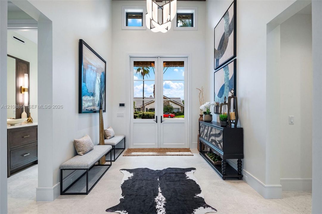 Double-entry glass paneled doors, high ceilings, geometric chandelier, clerestory windows, and light-toned tile flooring