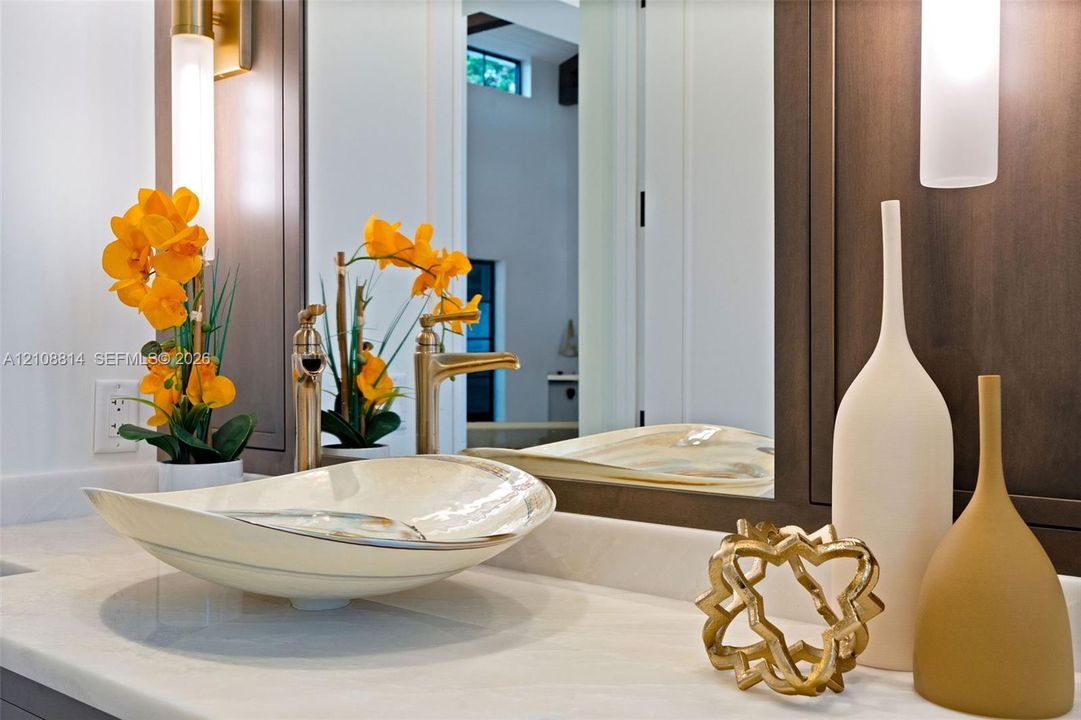 Vanity featuring a stone-surface countertop, vessel sink, metallic-finish faucet, framed mirror, and vertical wall-mounted lighting