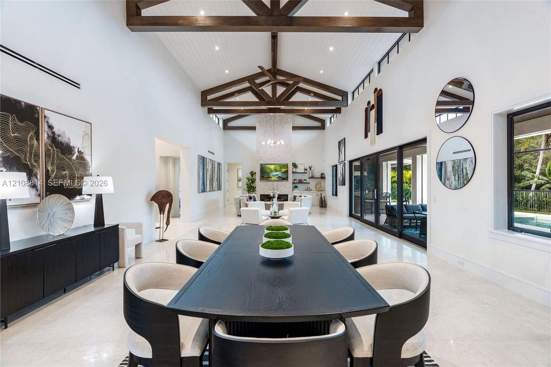 Vaulted ceilings with exposed wood beams, polished stone flooring, custom built-in cabinetry, floor-to-ceiling sliding glass doors, and a decorative tile fireplace surround