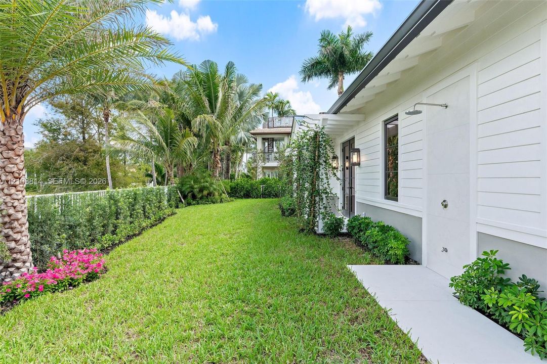 Exterior featuring horizontal lap siding, manicured lawn, established perimeter landscaping, palm trees, and a wall-mounted outdoor shower fixture