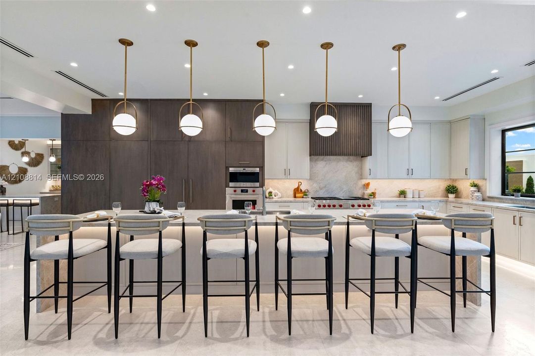 Kitchen featuring a large central island with waterfall-edge stone countertop, custom cabinetry, integrated professional-grade appliances, recessed lighting, and a series of globe-style pendant lights