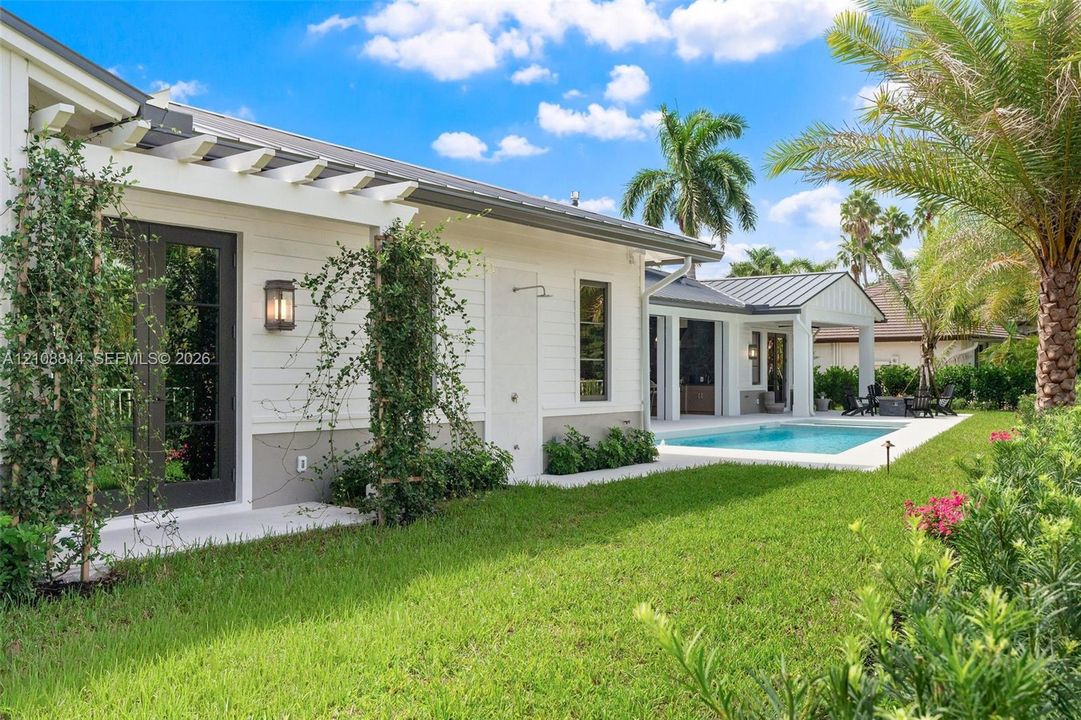 Exterior featuring white lap siding, a metal roof, pergola-covered patio, outdoor shower, and swimming pool