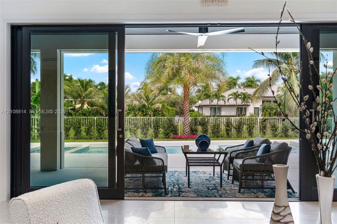 Large-format sliding glass doors, covered concrete patio, built-in ceiling fan, swimming pool, and privacy fencing