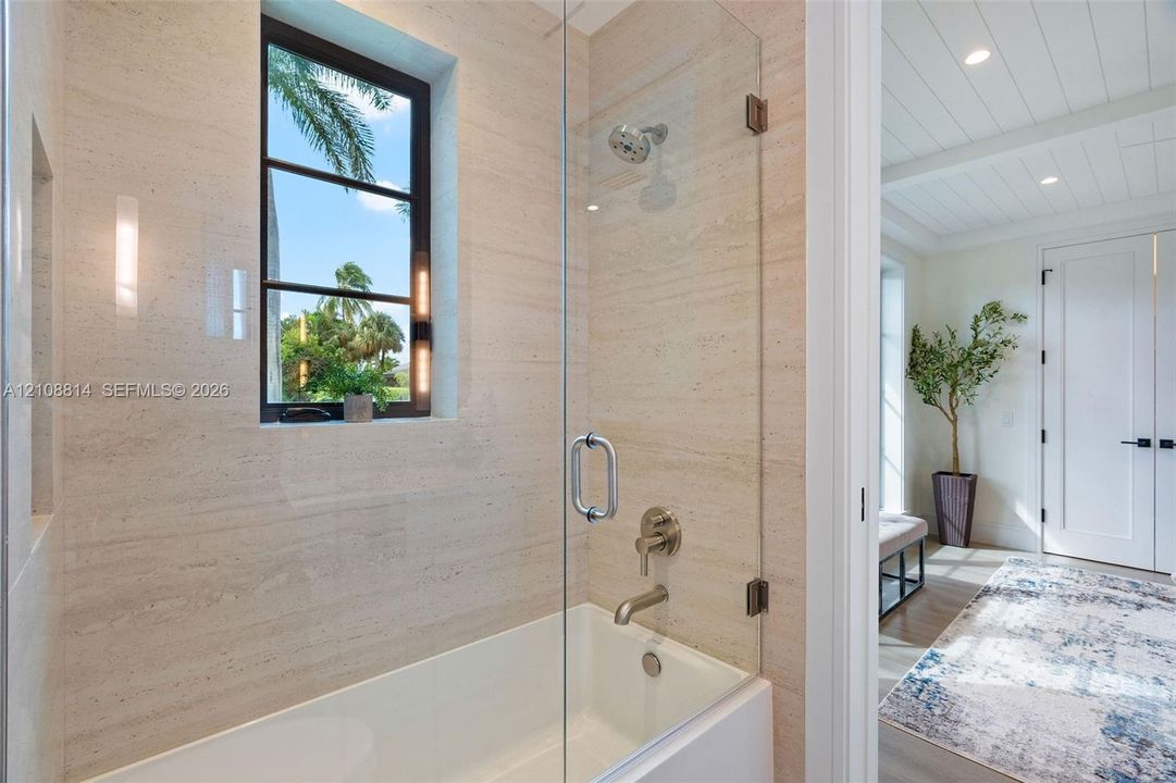 Bathroom featuring wall-to-wall natural stone tile, frameless glass shower enclosure, built-in recessed niche, and window with dark metal framing