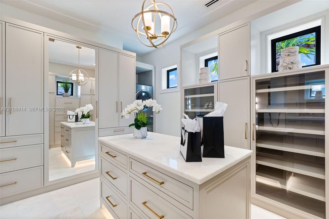 Custom built-in cabinetry with integrated lighting, central island with stone countertop, full-length mirror, glass-front display shelving, and orb-style metallic pendant light fixture