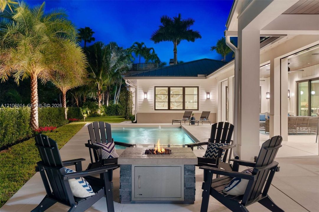 Covered patio featuring a concrete deck, built-in fire pit with stone-finish base, rectangular swimming pool, and landscape lighting