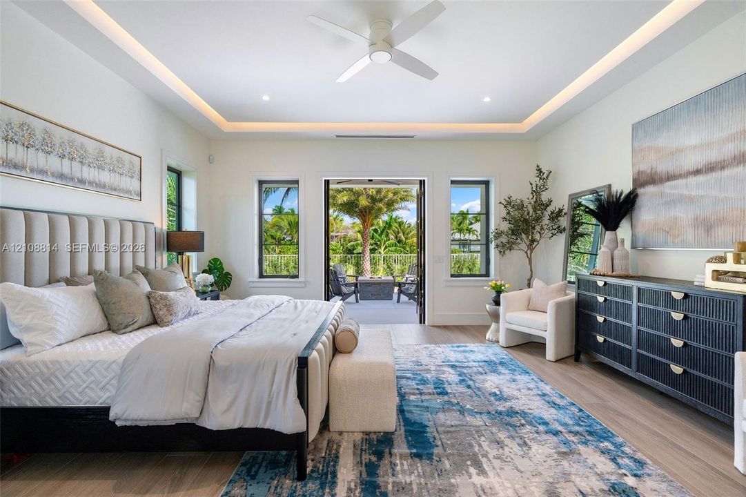 Bedroom featuring a tray ceiling with cove lighting, porcelain-finish flooring, a ceiling fan, and multi-pane windows with glass door access to an exterior area