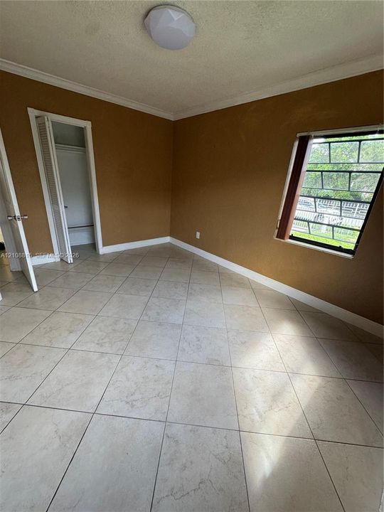 Room featuring large-format ceramic tile flooring, built-in closet with louvered bifold doors, and a window with security bars