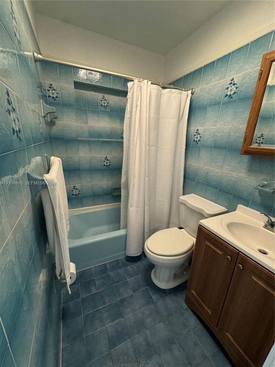 Bathroom featuring floral-patterned wall tiling, a built-in bathtub with a matching blue basin, a wood-finish vanity cabinet, and a wall-mounted medicine cabinet