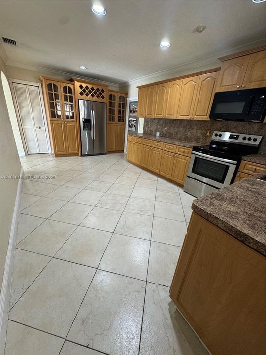 Kitchen featuring wood cabinetry, built-in wine storage, stone-finish countertops, stainless steel appliances, and large-format tile flooring set on a diagonal