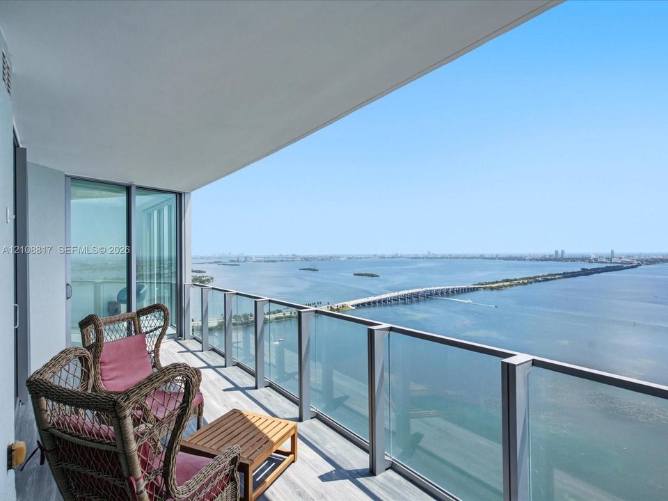 Covered balcony with a glass-panel railing, wood-finish flooring, and full-height sliding glass doors