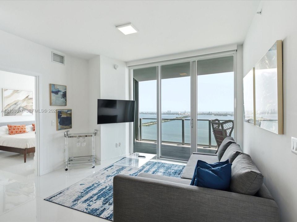 Floor-to-ceiling glass sliding doors with access to a private balcony, polished tile flooring, and panoramic water scenery