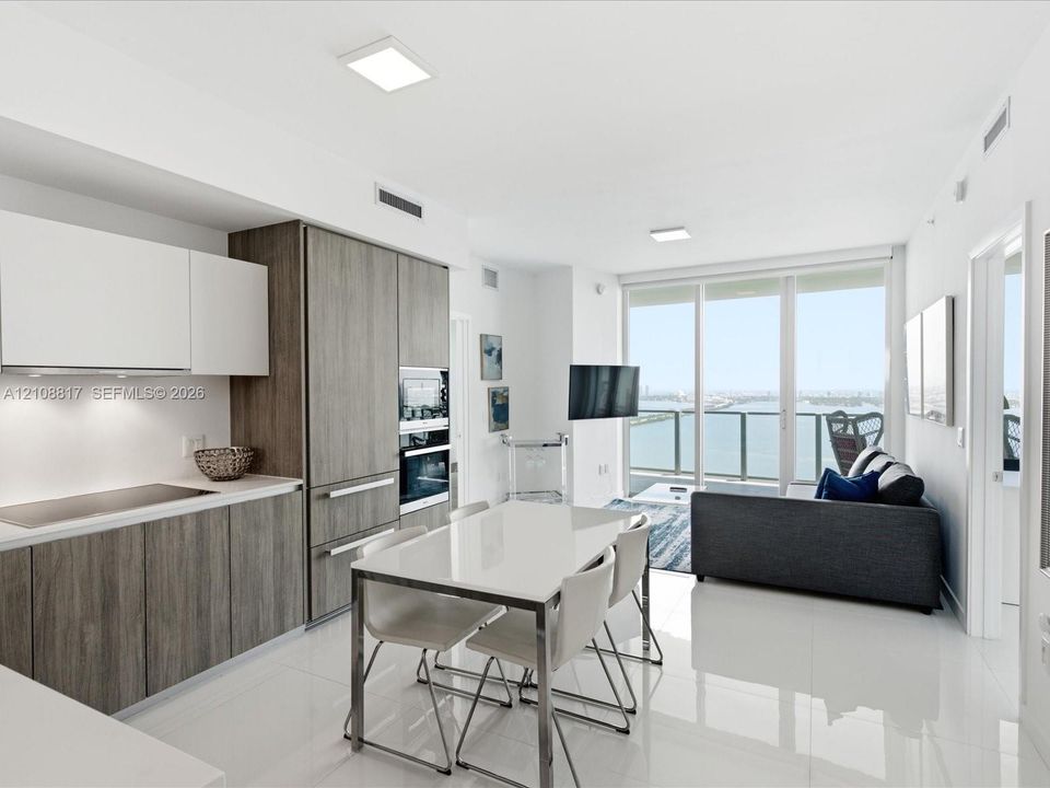 Kitchen featuring two-tone cabinetry with wood-finish and flat-panel white uppers, integrated appliances, white stone countertops, and polished tile flooring, extending toward floor-to-ceiling glass sliding doors opening to a balcony