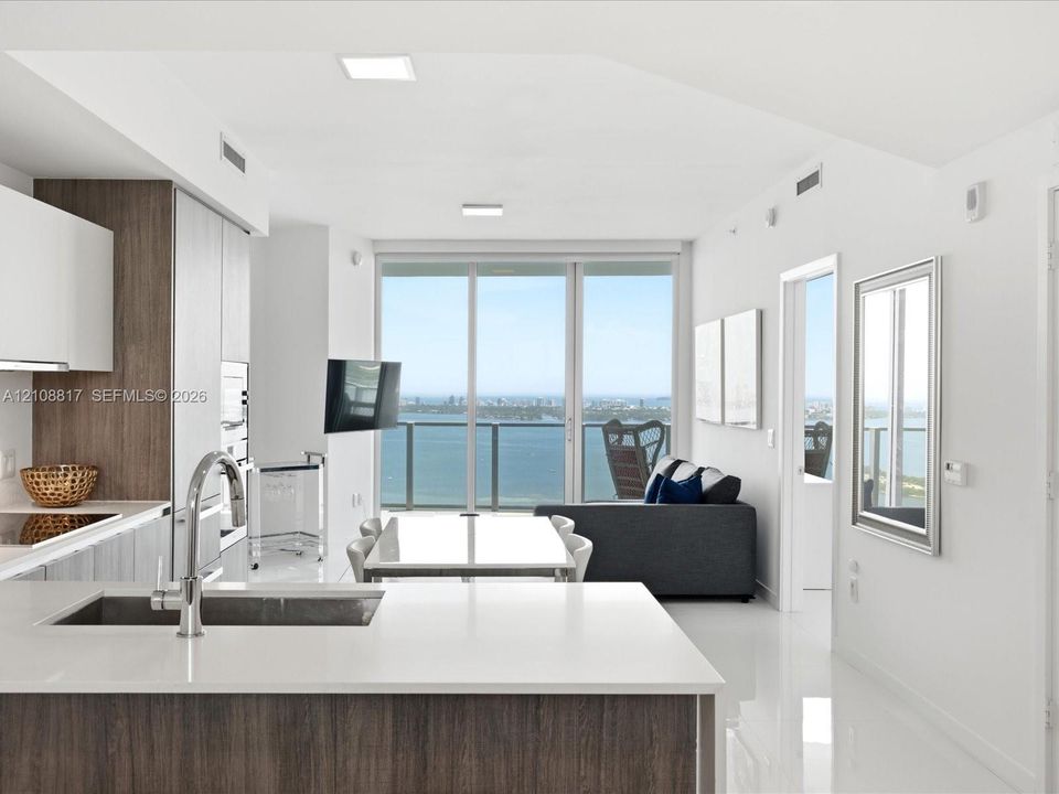 Contemporary kitchen featuring two-tone cabinetry, stone countertops, integrated stainless steel appliances, and polished tile flooring, accented by floor-to-ceiling glass sliding doors leading to a balcony