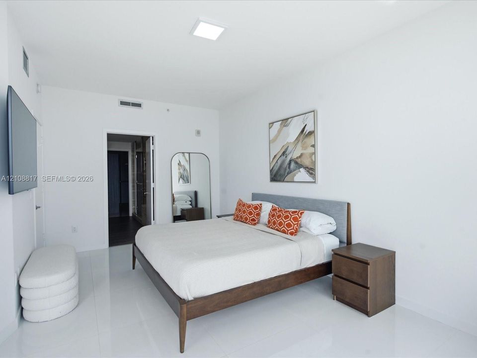Spacious room featuring high-gloss tile flooring, smooth white walls, recessed ceiling lighting, and a wall-mounted television
