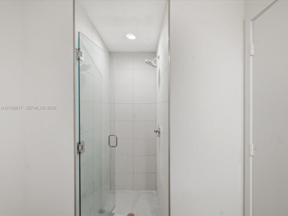 Walk-in shower featuring a frameless glass door, floor-to-ceiling white tile surround, mosaic tile flooring, and a chrome showerhead
