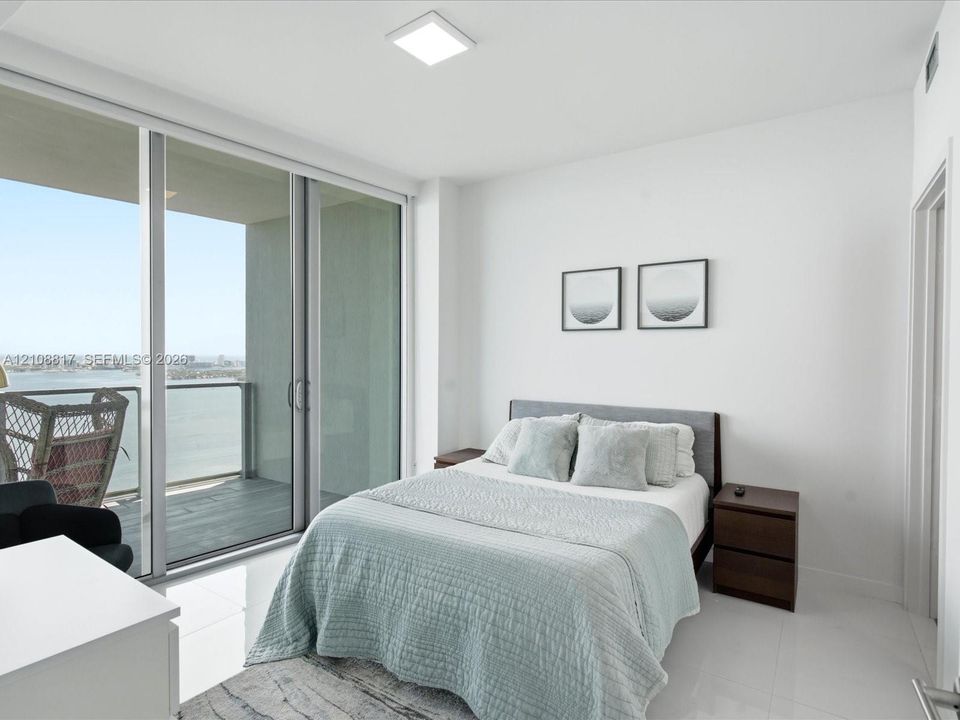 Floor-to-ceiling glass sliding doors opening to a private balcony, water scenery, and polished tile flooring
