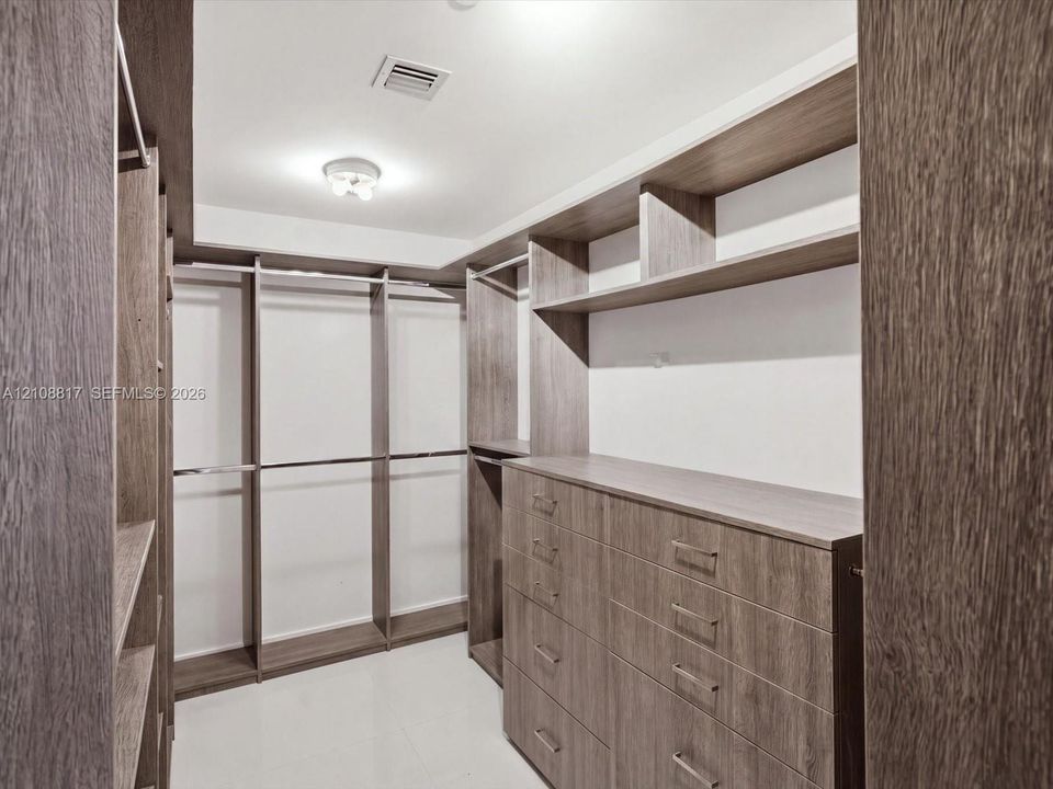 Walk-in closet featuring floor-to-ceiling wood-finish cabinetry, built-in shelving, integrated hanging rods, and a multi-drawer chest
