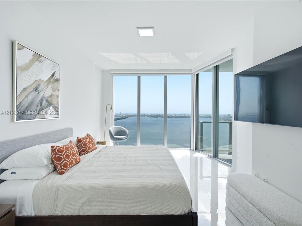 Floor-to-ceiling windows, polished tile flooring, and a private balcony featuring a water backdrop