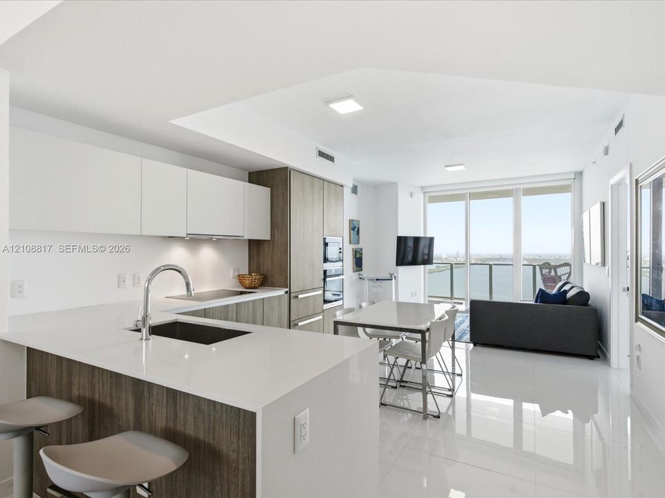 Kitchen featuring matte white cabinetry, wood-finish lower cabinetry, quartz countertops, integrated stainless steel appliances, and large-format tile flooring