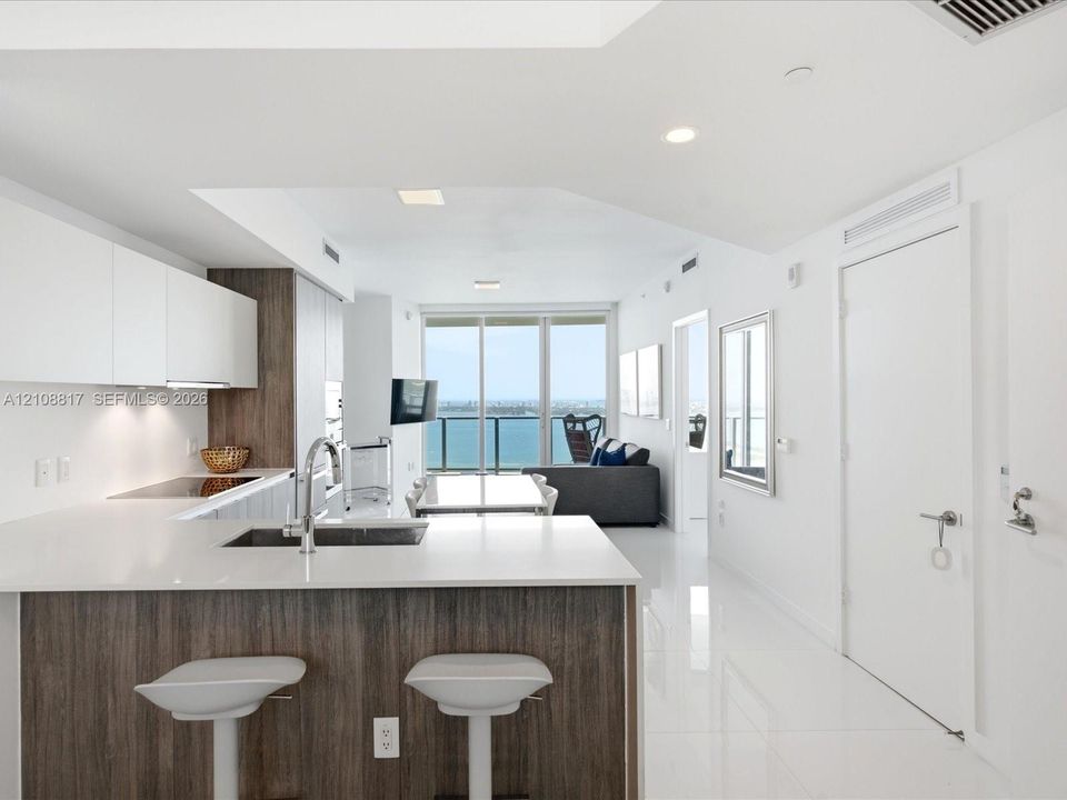 Kitchen featuring high-gloss cabinetry, wood-finish lower cabinets, stone countertops, and floor-to-ceiling glass sliding doors opening to a balcony