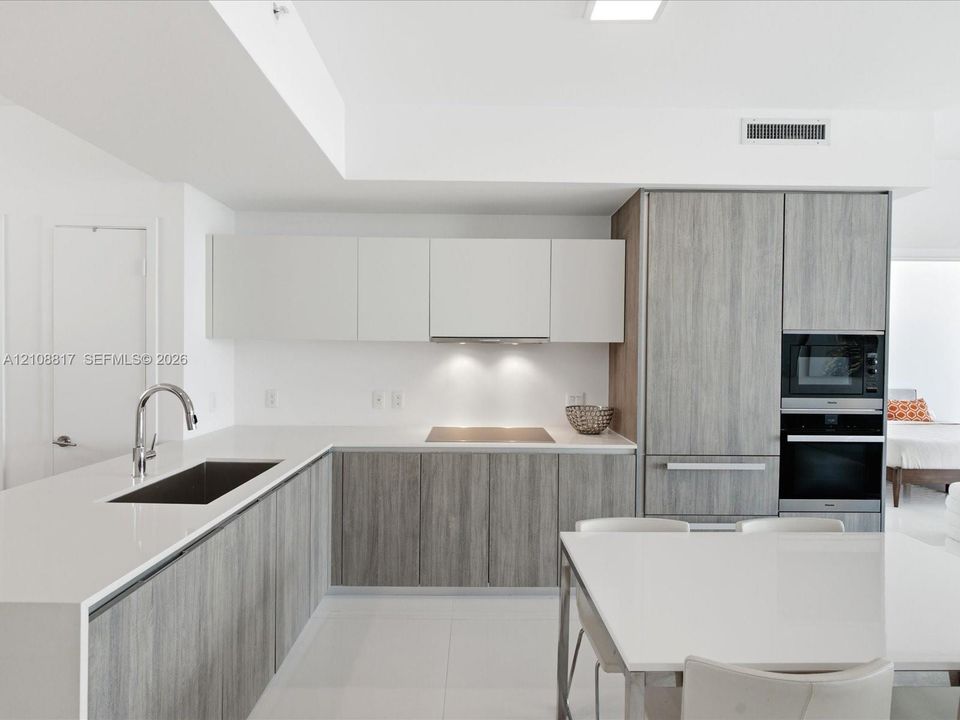 Contemporary kitchen featuring dual-tone cabinetry, quartz countertops, integrated stainless steel appliances, and a recessed stainless steel sink with a high-arch faucet